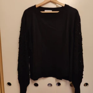 Svart stickad tröja med mönstrade ärmar - Svart stickad tröja från Jimmy Key med långärmade, detaljerade ärmar som har ett snyggt, upphöjt mönster. Tröjan har en rund halsringning och en loose passform som ger en chill vibe. Perfekt för dig som gillar stilrena plagg med en twist.