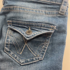 Blå bootcut jeans med slitningar - Snygga blå jeans från Ginatricot med bootcut passform och slitna detaljer på framsidan. Klassisk femficksmodell med dekorativ bakficka och kontrastsömmar. Jeansen har låg midja och är tillverkade i jeansmaterial med lite stretch.