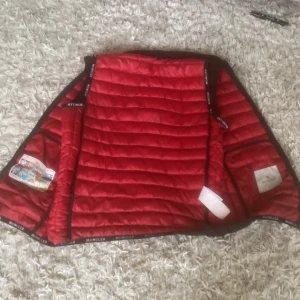 Svart och röd dunjacka från Moncler - Säljer en snygg dunjacka från Moncler med svart utsida och röd insida. Jackan har quiltad design, dragkedja och Moncler-logga på ärmen. Perfekt för dig som vill ha en stilren och varm jacka med exklusiv känsla. Passformen är normal och materialet är dun och syntet.