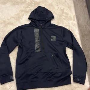 Nike Air Max marinblå hoodie L - Nike Air Max hoodie i marinblått med huva och stor magficka med dragkedja. Snygga Air Max-detaljer på bröstet, ärmslut och nederkant. Tillverkad i mjukt syntetmaterial, perfekt för chill eller träning. Långärmad och relaxed fit.