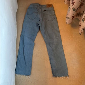 Lee ljusblå jeans W28 L32 med rå kant - Ljusblå jeans från Lee i modellen West, tillverkade av ekologisk bomull. Jeansen har rak passform, klassiska fem fickor och rå, fransig kant nedtill för en cool och avslappnad vibe. Perfekt för dig som gillar en enkel men snygg stil.