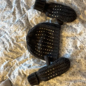 Svart stickad mössa med paljetter - Snygg mörkgrön stickad mössa med glittriga guldiga paljetter. Matchande vantar med paljetter ingår. Bra skick, gosigt tyg,inte sticksigt