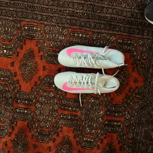 Nike mercurial ljusblå och rosa - Säljer ett par Nike fotbollsskor i ljusblå med snygga rosa detaljer och turkosa dobbar. Skorna har snörning och är tillverkade i syntetmaterial för lätt känsla på planen. Perfekta för dig som vill sticka ut med stilrena och sportiga skor på matchen. Jag säljer pågrund av att jag köpte dom till min lillebror men dom är för små för han, fotbollsskor har använts runt 7 gånger 