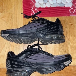 Nike Air Max Plus Tn Svarta Sneakers - Nike Air Max Plus Tn sneakers i svart och mörkgrå färg med synliga luftkuddar i sulan och coola detaljer på sidan. Ovandelen är i syntet och mesh med snörning och små silvriga swoosh-loggor. Platt sula och rund tå för skön komfort. Nypris 2200