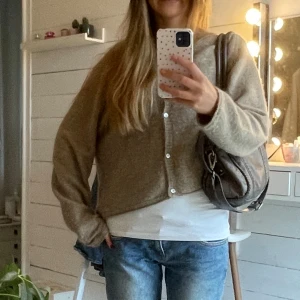 Beige kofta med knappar - Mysig beige kofta med knappar framtill och avslappnad passform. Koftan har lång ärm och är tillverkad i ett stickat material som känns både mjukt och skönt. Perfekt att slänga över en t-shirt för en chill look.