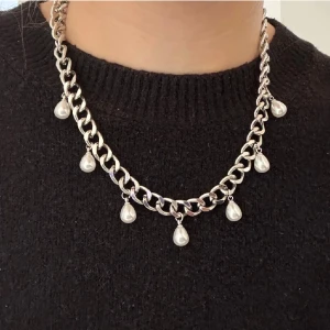 Chunky silverhalsband med pärldroppar - Stilrent halsband med grov silverfärgad kedja och hängande droppformade pärlor. Kedjan ger ett edgy intryck medan pärlorna tillför en elegant touch. Perfekt för dig som vill sticka ut med accessoarer som känns både trendiga och klassiska.