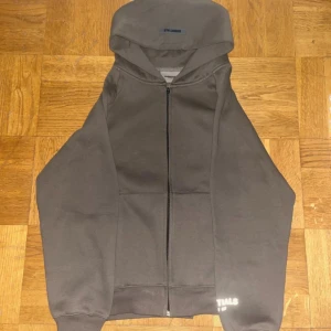 Grå Essentials Fear of God hoodie S - Säljer en grå hoodie från Essentials Fear of God i storlek S men passar också till personer med storlek M. Tröjan har dragkedja, huva och stora fickor framtill. Tillverkad i 100% bomull och har tydlig logga på ryggen. Perfekt för en chill och stilren look. 