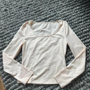 Ljusbeige långärmad topp - En stilren ljusbeige topp med lång ärm och rundad, djup urringning. Perfekt att matcha med jeans eller kjol för en clean look. Mjuk och skön i materialet, enkel att styla till olika outfits.