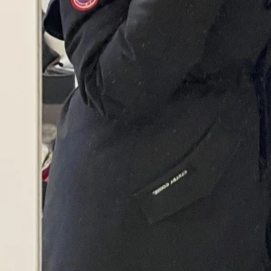rossclair parka canada goose - Säljer en svart dunjacka från Canada Goose med klassisk röd logga på ärmen och praktiska fickor med lock. Jackan är lång och har en stilren design som håller dig varm under kalla dagar.
