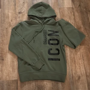 Grön hoodie DSQUARED2 ICON  - Snygg grön hoodie från DSQUARED2 med stor svart 'ICON'-print på framsidan och snörning vid huvan. Tröjan har lång ärm och lite slimmad passform, perfekt för dig som gillar grisch still eller annat och vill sticka ut med en fet logga. ‼️OBS köptes för 5000‼️