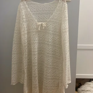 Vit spetsklänning med knyt och mönster - Superfin vit klänning i spets med v-ringning och söt knytning framtill. Klänningen har ett genomgående zickzack-mönster och är tillverkad i ett luftigt material som passar perfekt till varma dagar. Långa ärmar och lätt transparent.💞
