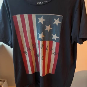 Mörkblå t-shirt - Väldigt snygg selected jeans T-shirt, trycket liknar chrome hearts amerikanska flagg tryck, säljer då jag tyvärr tröttnat på den. Hör av er vid frågor eller funderingar priset går att diskutera.