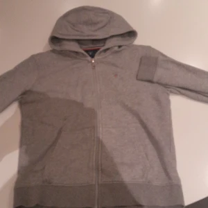 Grå hoodie med dragkedja - Säljer en enkel och stilren grå hoodie med dragkedja och huva. Tröjan har långa ärmar och är perfekt för chill dagar. Mjuk och skön, passar dig som gillar basic streetstyle.