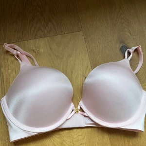 Ljusrosa satin bombshell bh från Victoria's Secret - Supersnygg ljusrosa bh från Victoria's Secret i glansigt satinmaterial. Bh:n har formpressade kupor och justerbara axelband, samt en liten guldfärgad detalj framtill. Perfekt för dig som gillar en feminin och stilren look. Helt ny