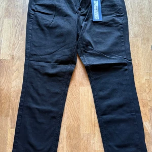 Svarta byxor från Atelier Gardeur - Svarta byxor från Atelier Gardeur, modell ZURI-0. Klassisk rak passform med normal midja och snygga fickdetaljer både fram och bak. Materialet är mjukt och har en lätt stretch för extra komfort. Perfekta för en clean och stilren look. Ordinarie pris 1027kr