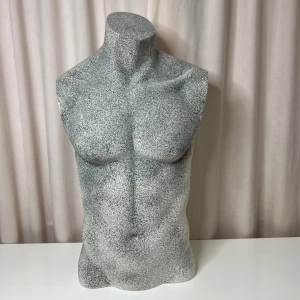 Fantasy EF-3 Mannequin Torso - Stilren och robust herrmannekäng i gråmelerad finish, modell EF-3 från Fantasy. Passar utmärkt för visning av kläder eller accessoarer. Skicket är mycket gott med minimalt slitage, inga synliga sprickor eller större märken. Monteringsfäste på axeln för enkel uppställning.