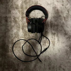 HyperX Cloud Alpha - HyperX Cloud Alpha gaming headset med kabelanslutning och avtagbar mikrofon. Robust design med röd aluminiumram och bekväma öronkuddar. Headsetet är i gott skick med mindre tecken på normalt bruk, perfekt för spel och kommunikation.