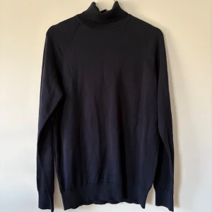 Svart polotröja från Bläck, M - Svart polotröja från Bläck i storlek M. Tröjan har en klassisk hög krage och är långärmad med ribbade muddar vid hals och ärmslut. Materialet är mjuk bomull som känns skönt mot huden. Perfekt för dig som gillar stilrena och enkla plagg. Ny utan prislapp!