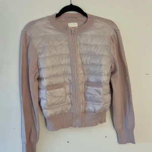 Rosa quiltad cardigan jacka - Snygg rosa cardigan jacka med quiltad framsida och två fickor. Jackan har dragkedja framtill och ribbade muddar vid hals, ärmslut och nederkant. Materialmix med stickade ärmar och quiltad kropp ger en chill och modern look.