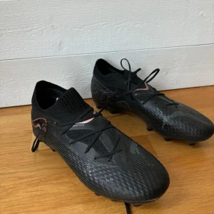 Svarta fotbollsskor från Puma strl 39 - Säljer ett par svarta fotbollsskor från Puma i storlek 39. Skorna har snörning, låg profil och mönstrad ovansida i syntetmaterial. Yttersulan har fasta dobbar för bra grepp på planen. Andvända ungefär 6-7 gånger. 