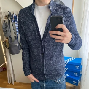 Marinblå kofta från Massimo Dutti - Snygg marinblå stickad kofta från Massimo Dutti med grov ribbad krage och knappstängning hela vägen. Koftan har långärmad passform och är tillverkad i mjukt bomullsmaterial. Perfekt för dig som gillar stilrena och bekväma plagg.