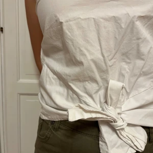 Vit linnetopp med korsade band - Säljer en vit linnetopp med snygga korsade band i ryggen och knytning i sidan. Toppen är ärmlös och har en clean, enkel look med rund halsringning. Perfekt för dig som gillar minimalistisk stil och vill ha något fräscht till sommaren.