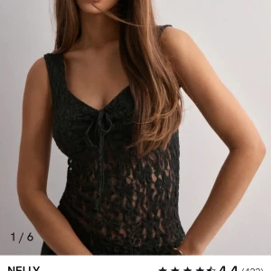 Svart spetslinne med knyt från Nelly - Svart ärmlös linnetopp i spets från Nelly med v-ringning och knyt framtill. Toppen är figurnära och har ett transparent blommönster i spetsmaterial som ger en cool och trendig look.