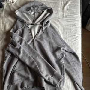 J Lindeberg kofta - Säljer en grå hoodie med huva och snörning, hel dragkedja framtill och fickor. Baksidan har ett stort tryck i mörkgrått som ger en cool look. Skriv om du har funderingar!😄