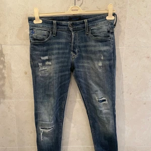 Blå slitna jeans från Jack & Jones - Snygga blå jeans från Jack & Jones i storlek 29/32 med slitningar och trasiga detaljer på benen. Modellen har klassisk femficksdesign, gul kontrastsöm på bakfickorna och en smal passform som sitter riktigt bra. Perfekt för dig som gillar en cool och avslappnad stil.