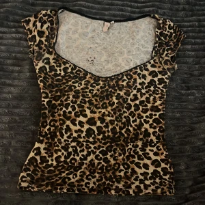 Leopardmönstrad topp från Nelly - Säljer en slim leopardmönstrad topp från Nelly i storlek S. Toppen har korta ärmar, v-ringad hals och är gjord i mjuk, stretchig polyester. Färgerna går i beige, brun och svart med ett djärvt leopardmönster som sticker ut. 