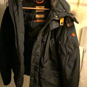 Parajumpers Right Hand Jacka - Exklusiv Parajumpers-jacka i svart med äkta päls på luvan. Jackan är varm, slitstark och perfekt för kalla vinterdagar. Klassisk modell med flera praktiska fickor, dragkedja och Parajumpers ikoniska patch på ärmen. Köpt på NK i Göteborg , vilket garanterar äkthet och kvalitet.