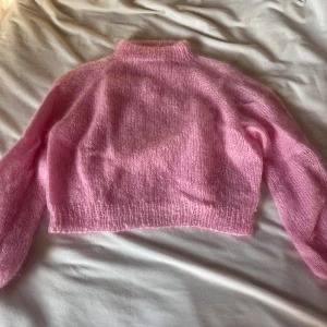 Ljusrosa stickad croppad tröja - Supermjuk och fluffig ljusrosa stickad tröja med croppad passform och hög hals. Perfekt för lager-på-lager och ger en söt vibe till din outfit. Långa ärmar och ribbade kanter för extra mysfaktor.