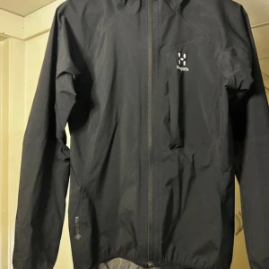 Svart vindjacka Haglöfs Gore-Tex  - Lätt, minimalistisk skaljacka i vattentätt, vindtätt och ventilerande Gore-Tex Paclite-material (28 000 mm vattenpelare). Åtsittande passform.  Haglöfs L.I.M Critus Jacket är en lätt och smidig jacka som lämpar sig för aktiv vandring, och den passar även för vardagsbruk under regniga dagar. Jackan tar lite utrymme när den är nedpackad. Köpt för ca 3 år sen för 2199 kr. 
