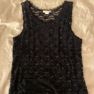 Svart spetslinne från Gina Tricot - Säljer ett svart ärmlöst linne från Gina Tricot i storlek 170. Toppen är helt i spets och perfekt med en lite kortare tröja över så det sticker ut lite spets. 