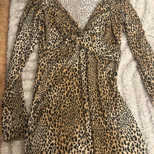 Leopardmönstrad kortklänning H&M - Snygg kort klänning från H&M med leopardmönster i beige, svart och brunt. Klänningen har lång ärm, v-ringad urringning och figurnära passform. Perfekt för dig som vill sticka ut med ett djurmönstrat plagg.