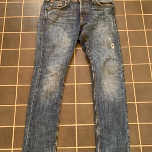 Blå jeans från Jack & Jones - Säljer ett par blå jeans från Jack & Jones med klassisk femficksdesign och snygga slitningar på framsidan. Jeansen har raka ben och är tillverkade i bomull med en autentisk denimkänsla. Perfekta för dig som gillar en avslappnad och tidlös look. 