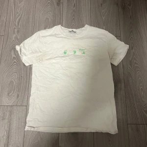 Vit Off-White t-shirt med grön print - Säljer en vit t-shirt från Off-White med grön logga framtill och stor grön grafisk print på ryggen. Klassisk passform och rund hals. Perfekt för dig som gillar streetwear och vill sticka ut med en ikonisk design.