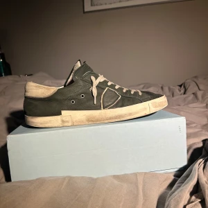 Philippe Model PRSX gröna sneakers - Säljer ett par Philippe Model PRSX Low Man sneakers i mörkgrön nubuck med vita detaljer och snörning. Snygg vintage-inspirerad look med slitna vita sulor och rund tå. Märket syns på plösen och insidan. Perfekt för dig som gillar exklusiva och unika sneakers. Perfekt nu för vintern då dem är varma och täta, pris kan diskuteras vid rätt köpare, finns några defekter i insidan av skon men som absolut inte syns när du sätter på dig skon 