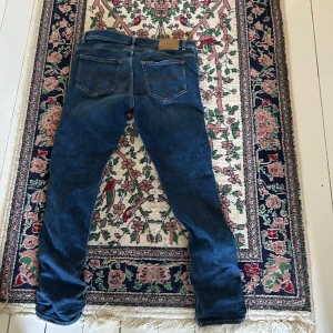 Blå tiger of sweden jeans - Säljer ett par blå tiger of sweden jeans med slim fit och klassisk femficksdesign. Jeansen har en snygg tvättad look, normal midja och raka ben med lätt tapered passform. Materialet är stretchigt jeans och de har tiger of sweden-logga på läderpatchen bak.