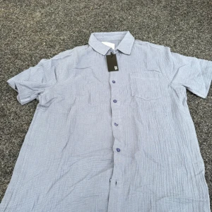 Ljusblå kortärmad skjorta från 157 - Snygg ljusblå skjorta från 157 i bomull med korta ärmar och klassisk krage. Skjortan har knappar framtill och en bröstficka. Perfekt för en chill och stilren look.