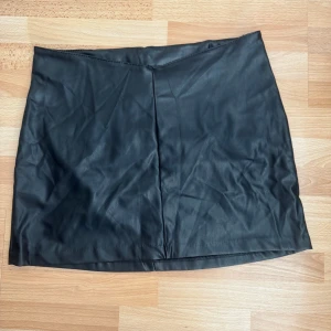 Ny. Svart skinnimitation kjol H&M Divided - Svart kort kjol i skinnimitation från H&M Divided. Enkel och stilren design med rak passform och diskret söm framtill. Perfekt för dig som gillar en edgy look och vill ha en klassisk bas i garderoben.