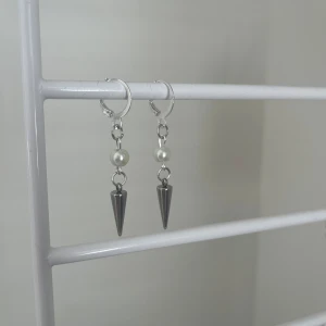 Silvriga örhängen med pärlor och spikes - Snygga örhängen i silverfärg med rund vit pärla och en cool konformad spike som hänger ned. Perfekt för dig som gillar edgy detaljer och vill sticka ut lite extra. Passar till både street och trendiga outfits. I rostfritt stål och handgjort