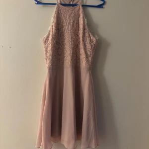 Ljusrosa spetsklänning från NLY Trend - Supersöt ljusrosa kortklänning från NLY Trend med spets upptill och flowy kjol. Hög halsringning och ärmlös design ger en fräsch look. Dragkedja bak för enkel påklädning. Perfekt för dig som gillar romantiska detaljer och en feminin stil.