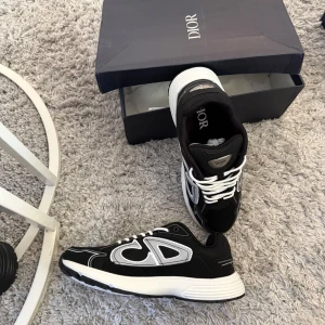 Svarta Dior sneakers med vit sula - Säljer ett par svarta Dior sneakers med vit och grå detalj på sidan och tjock vit sula. Skorna har snörning med vita skosnören och tydlig Dior-logga både på plösen och innersulan. Materialmix av textil och syntet ger en modern vibe.