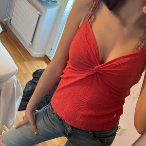 Röd twistad linnetopp med smala axelband y2k - Säljer en snygg röd linnetopp med twistad detalj framtill och smala axelband. Toppen har en lätt plisserad struktur och djup v-ringning. Perfekt att styla med jeans eller kjol för en trendig look.