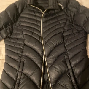 Svart dunjacka från Craft, M - Säljer en svart dunjacka från Craft i storlek M. Jackan har snygg quiltad design, dragkedja framtill och långärmade ärmar. Perfekt för kyliga dagar och har en sportig look med diskreta detaljer.