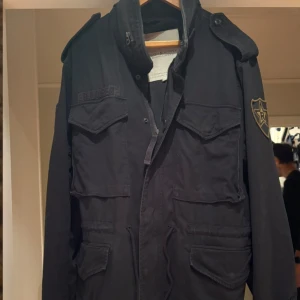 Ralph lauren denim&supply army jacket - Svart army/field jacka från Denim & Supply Ralph Lauren med coola patchar på ärmarna och flera stora fickor framtill. Jackan har snörning i midjan, axelklaffar och dragkedja med knappslå. 
