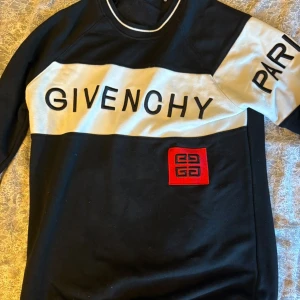 Givenchy svartvit sweatshirt - Svart och vit sweatshirt från Givenchy med stor logga över bröstet och ärmen samt röd patch med Givenchy-symbol på magen. Tröjan har rund halsringning med vit kant och långa ärmar. Perfekt för dig som gillar streetstyle och designerplagg.