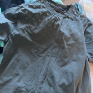 Louis vetton T-shirt  - Snygg mörkgrå t-shirt med diskret mönster över axlar och bröst. Klassisk rund halsringning och korta ärmar. Perfekt för dig som gillar stilrena plagg med en twist.