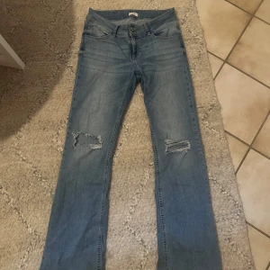 Ljusblå bootcut jeans från Nelly - Säljer ett par ljusblå jeans från Nelly med bootcut passform och slitna detaljer vid knäna i storlek 40 men passar även 38. Jeansen har dubbla knappar i midjan och klassisk femficksdesign. Perfekta för dig som gillar en avslappnad och trendig look. Köpte för 699 och säljer för 450 pågrund av slitna delen längst ned vid benen men annars är de som nya 